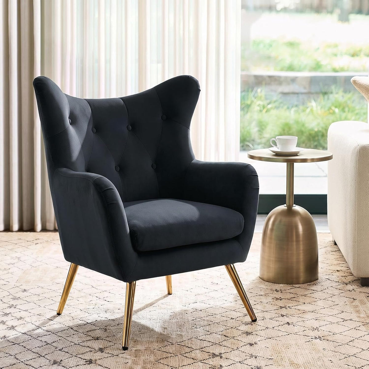 Dark navy velvet wingback chair shown beside a gold side table with a teacup in a sunlit window setting.
