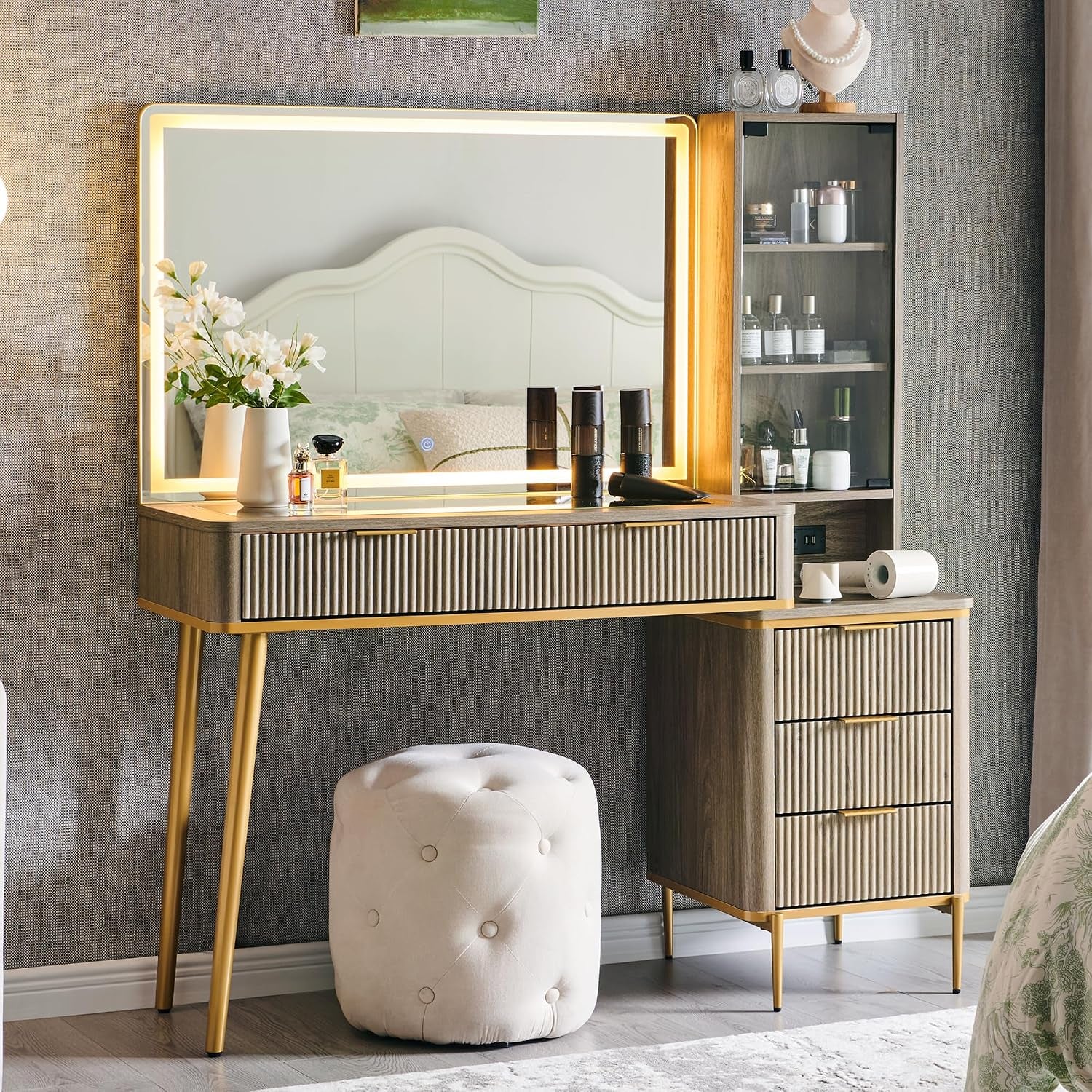 Alternate styled room view of the illuminated mirror vanity with glass-front shelving and a padded stool.