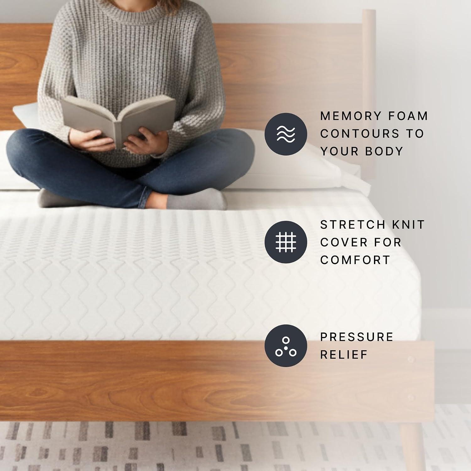 Person sitting cross-legged reading on a white mattress placed on a wooden platform bed.