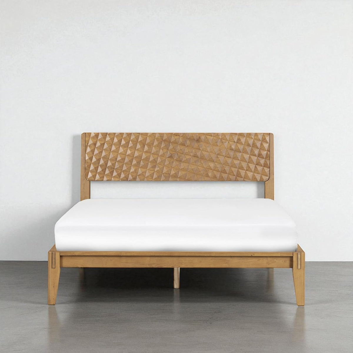 Front-facing bed in a honey-toned wood finish with carved geometric headboard on a concrete floor