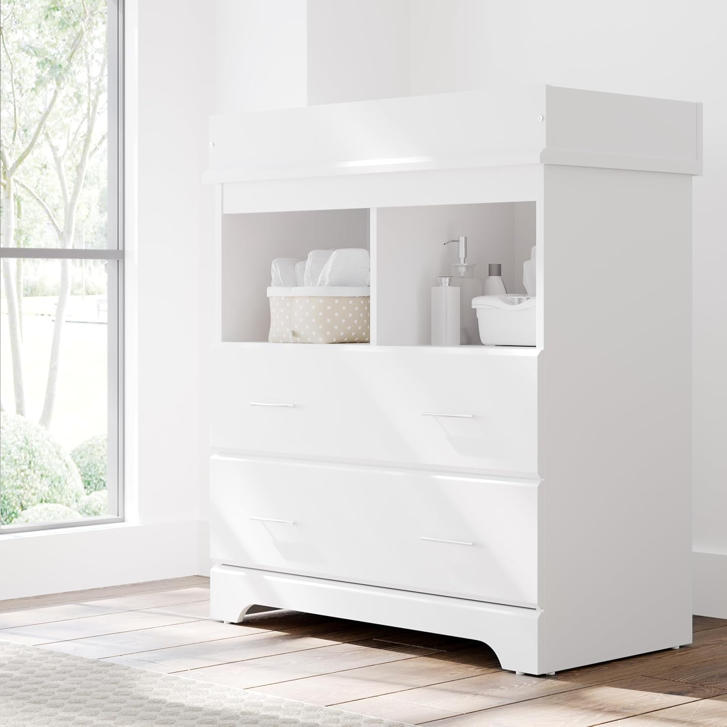 White changing chest staged in a bright nursery by a window on hardwood floor, angled front view