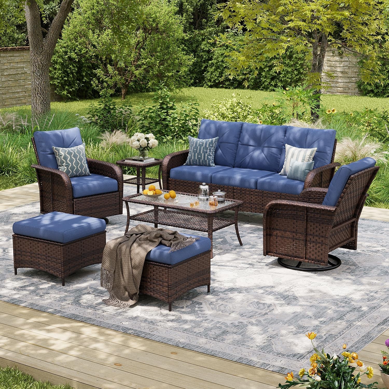 Patio set staged on rug outdoors with blue seat cushions, sofa, swivel chairs, ottomans and tables