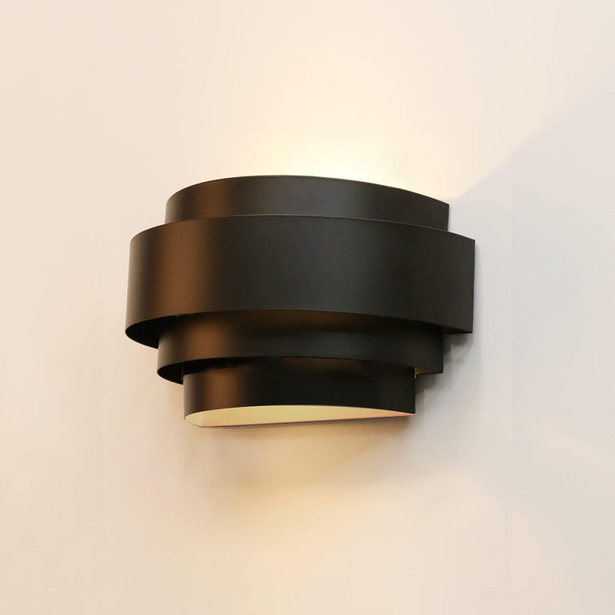 Close side view of a single black layered wall sconce showing concentric curved metal bands and warm light.