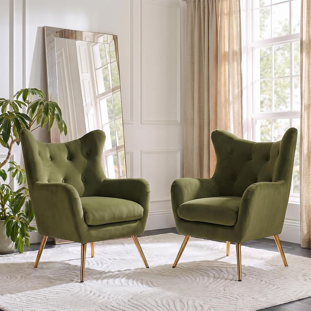 Pair of olive-green velvet wingback chairs with button tufting staged by a window and houseplant.