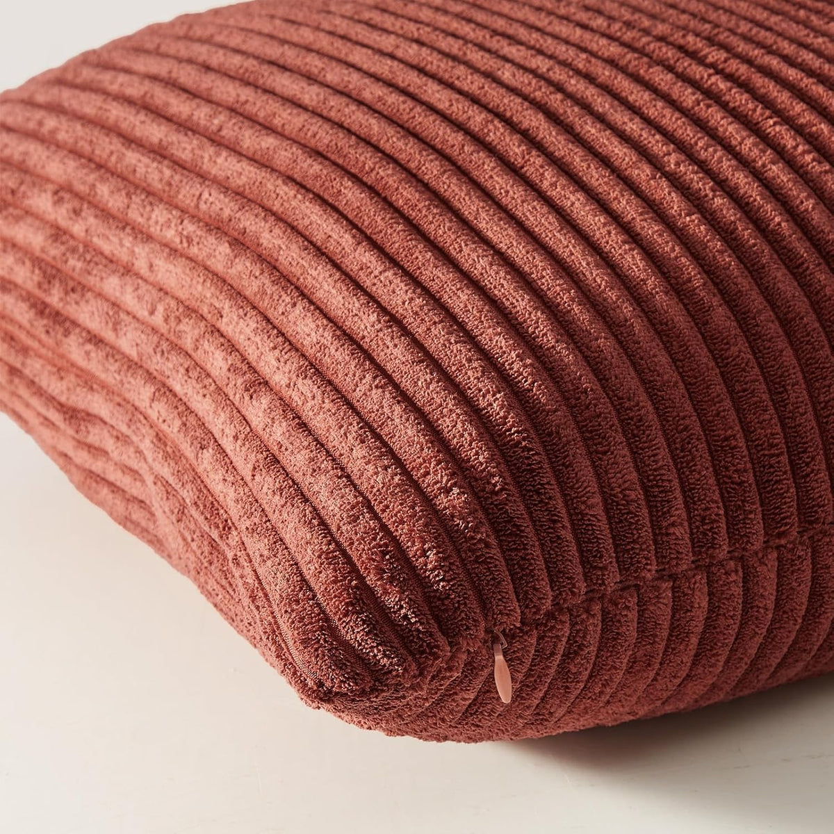 Macro close-up of rust-colored corduroy pillow cover showing vertical ribbed texture and an invisible zipper pull