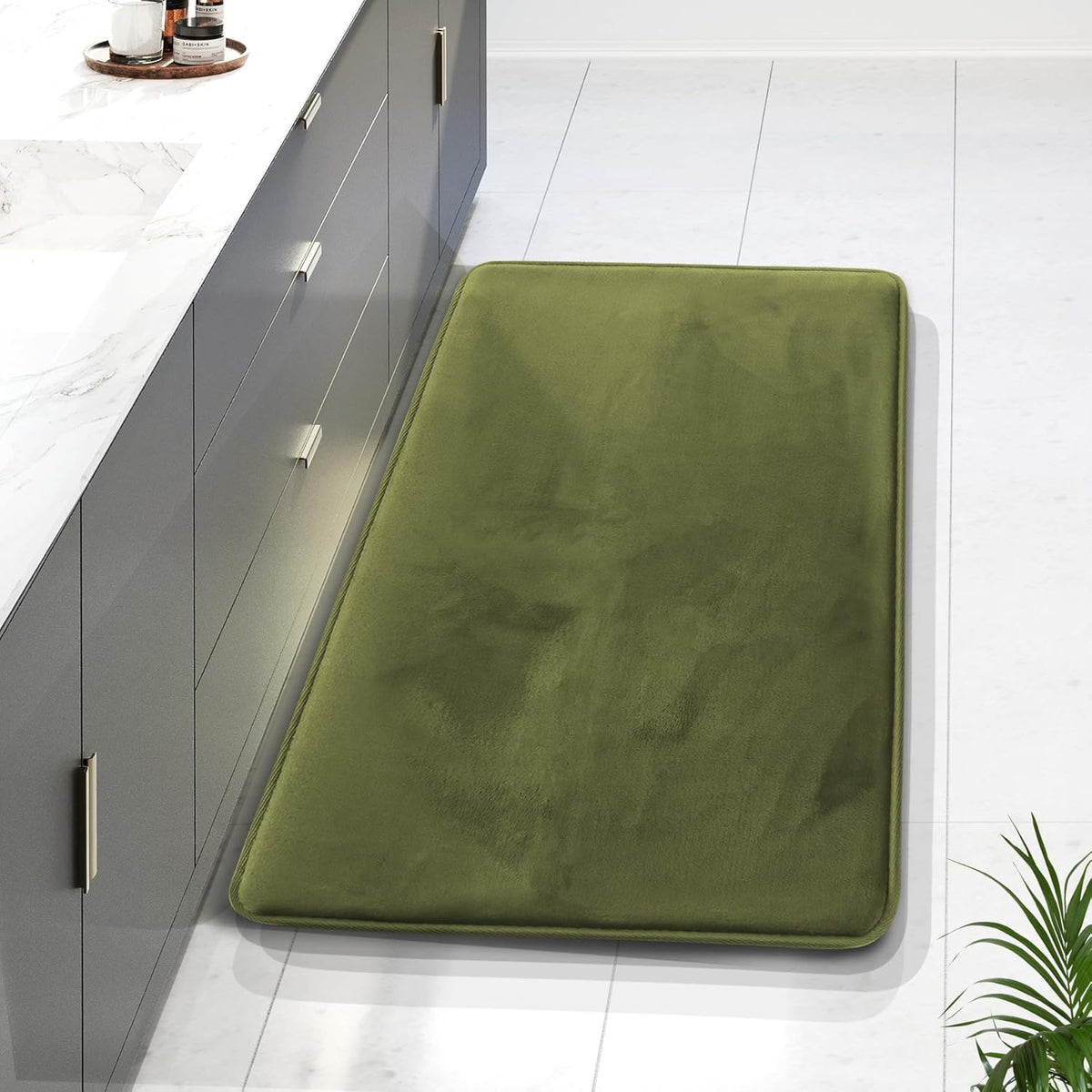 Angled view of a single olive-green long rectangular rug beside a gray vanity, with a small floor plant visible at the