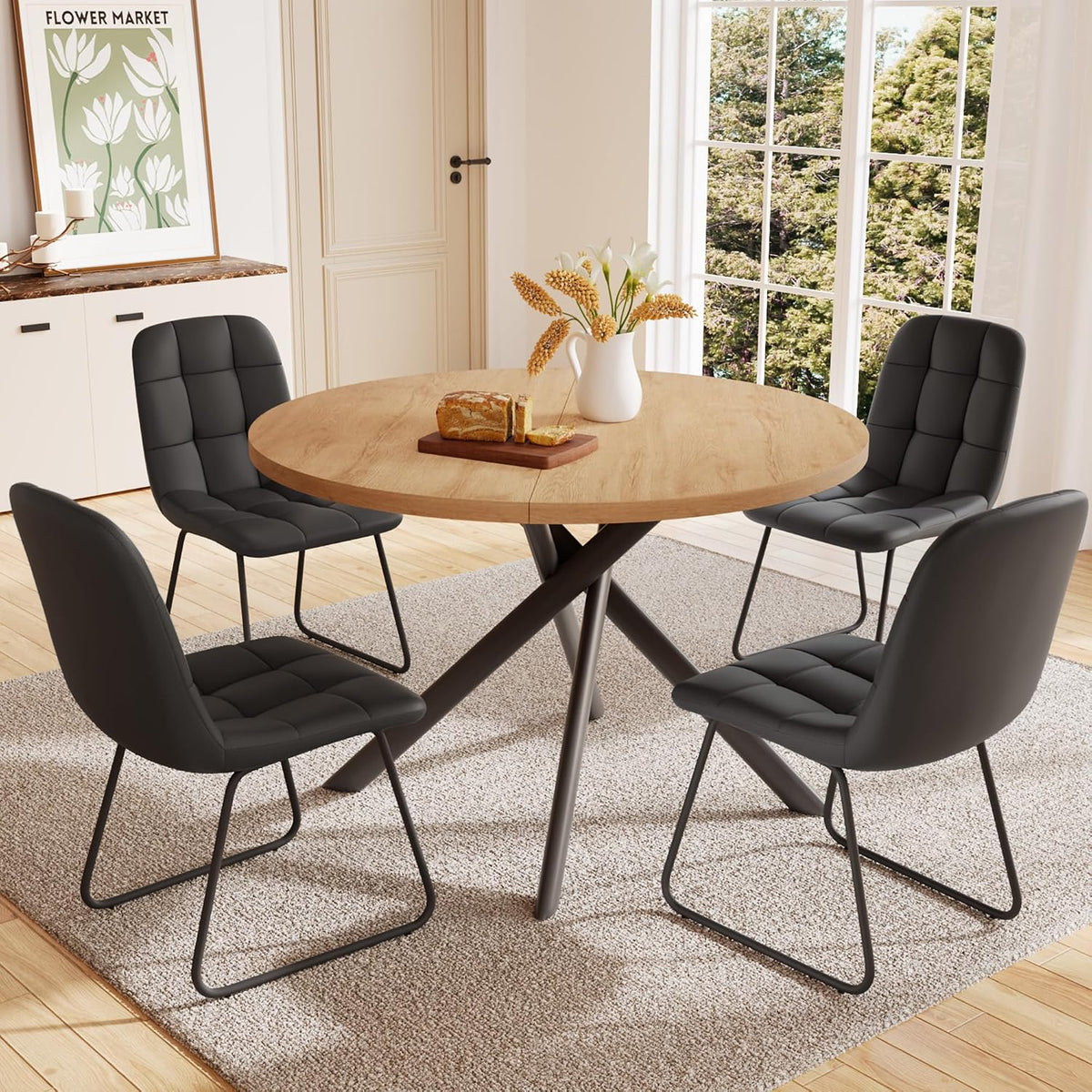 Round light-wood dining table surrounded by four black upholstered U-shaped chairs.