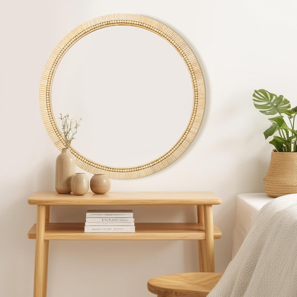 Round rattan mirror mounted above a light wood console table topped with three ceramic vases and books below.