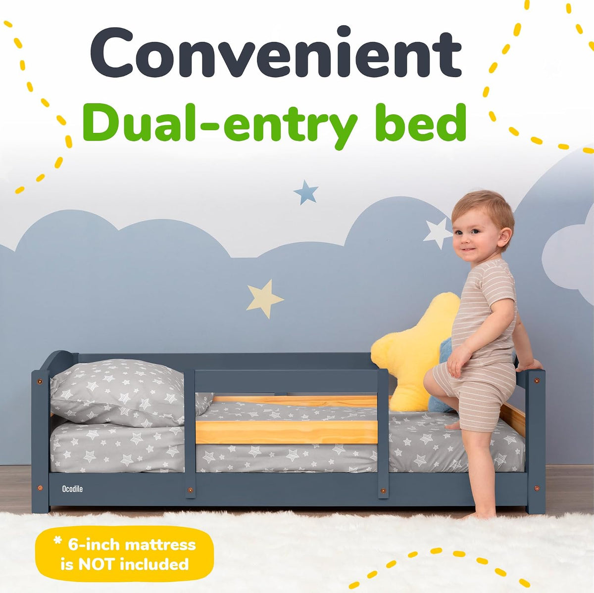 Toddler stepping into a low dark-gray wooden bed with star-pattern bedding and cloud-and-star wall backdrop.