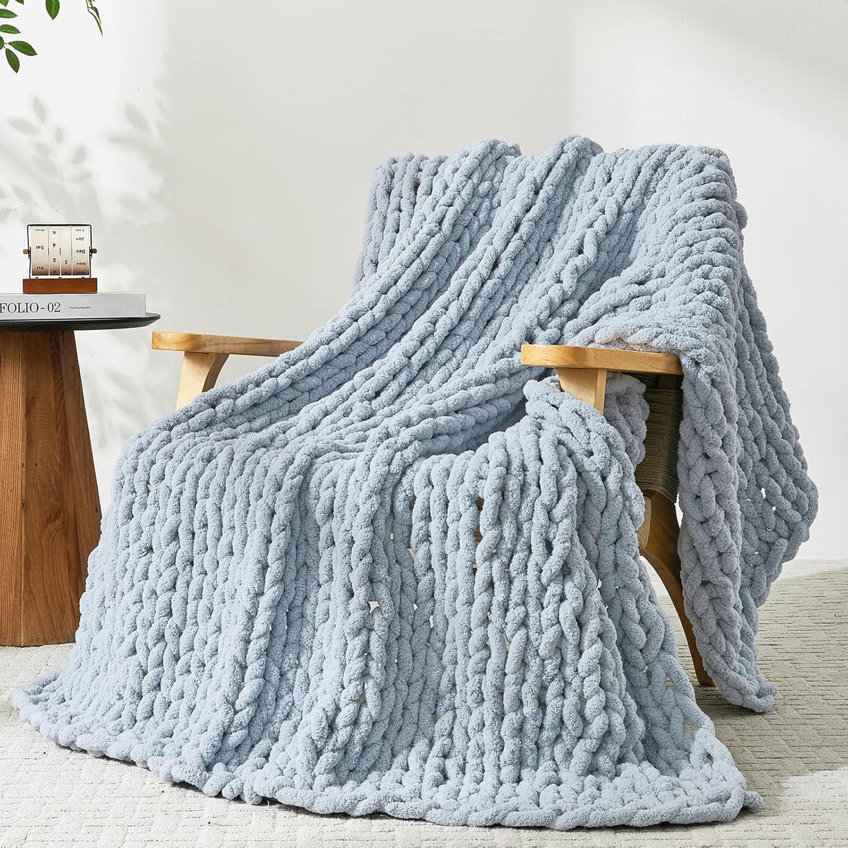 Pale blue chunky knit throw draped over a wooden armchair, pooling onto a light rug.