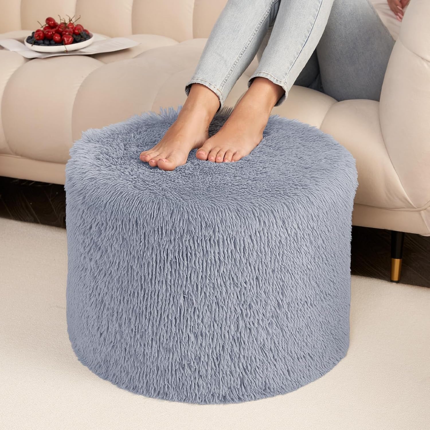 Front view of a blue-gray round pouf with bare feet resting on top beside a cream sofa.