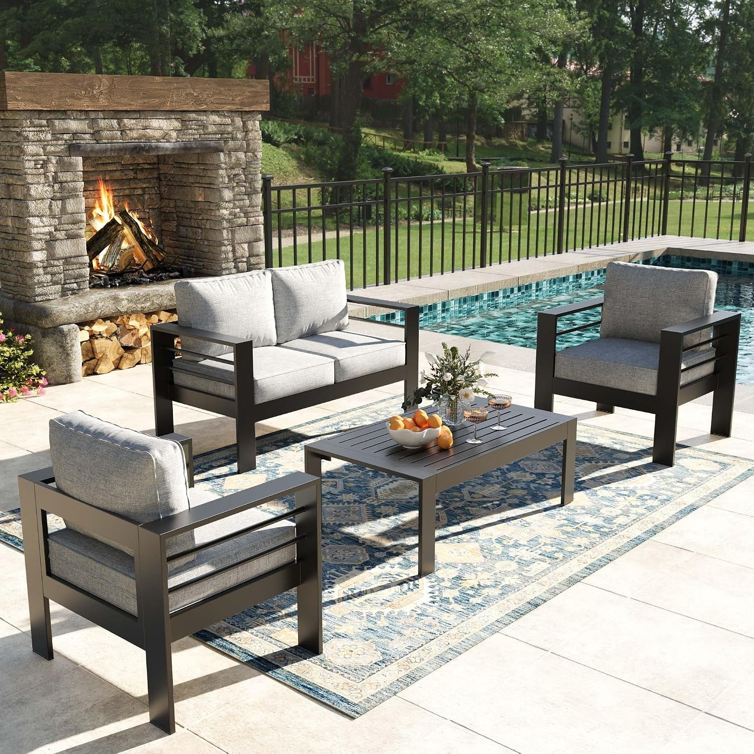 Patio set with two armchairs and a two-seat loveseat around a low slatted coffee table by a pool and stone fireplace.