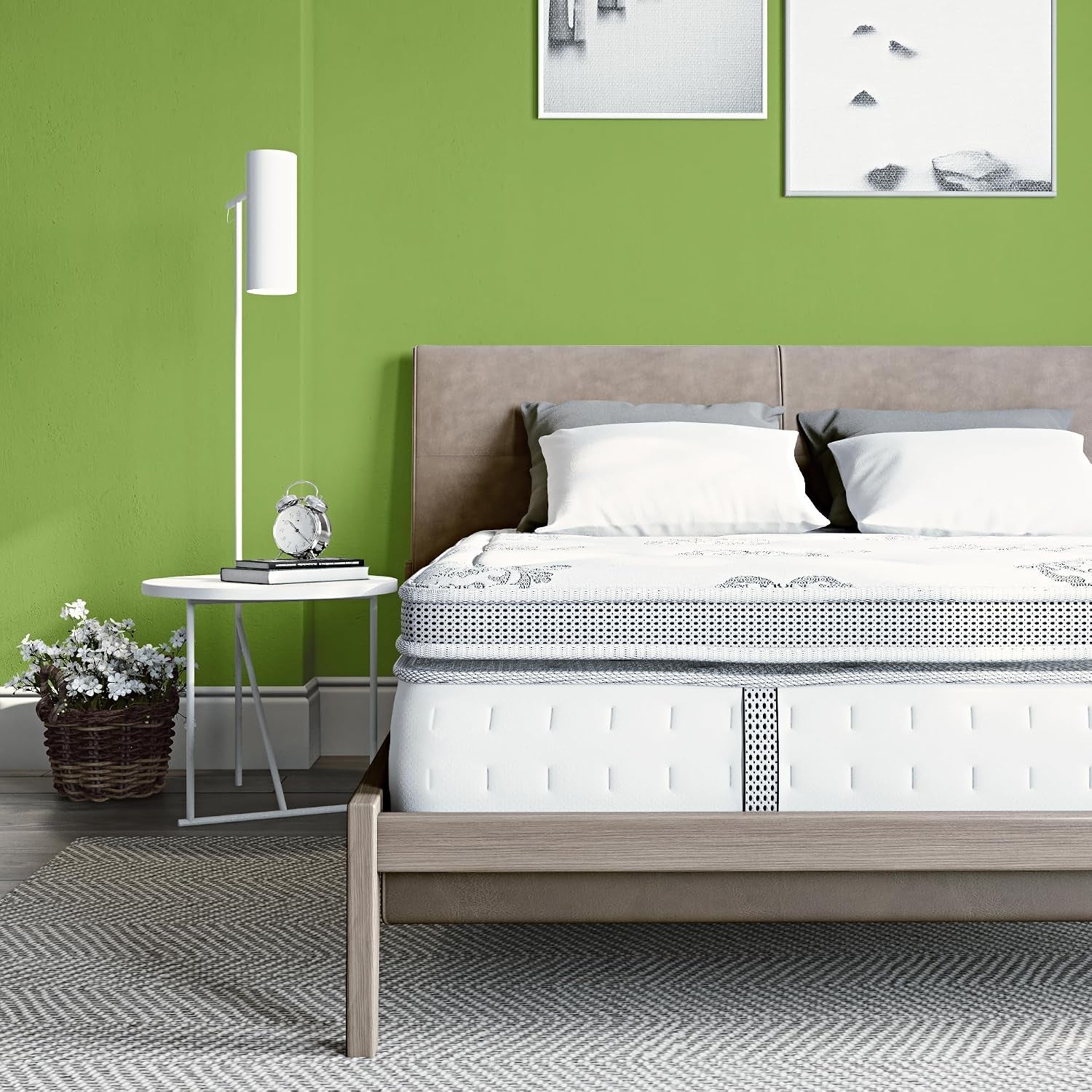 Side-framed view of the mattress on a light wood platform, with a round white side table and woven plant basket.