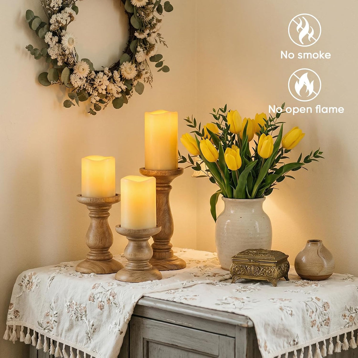 Three lit ivory pillar candles on wooden candlesticks beside a vase of yellow tulips and a decorative wreath, indoor view.