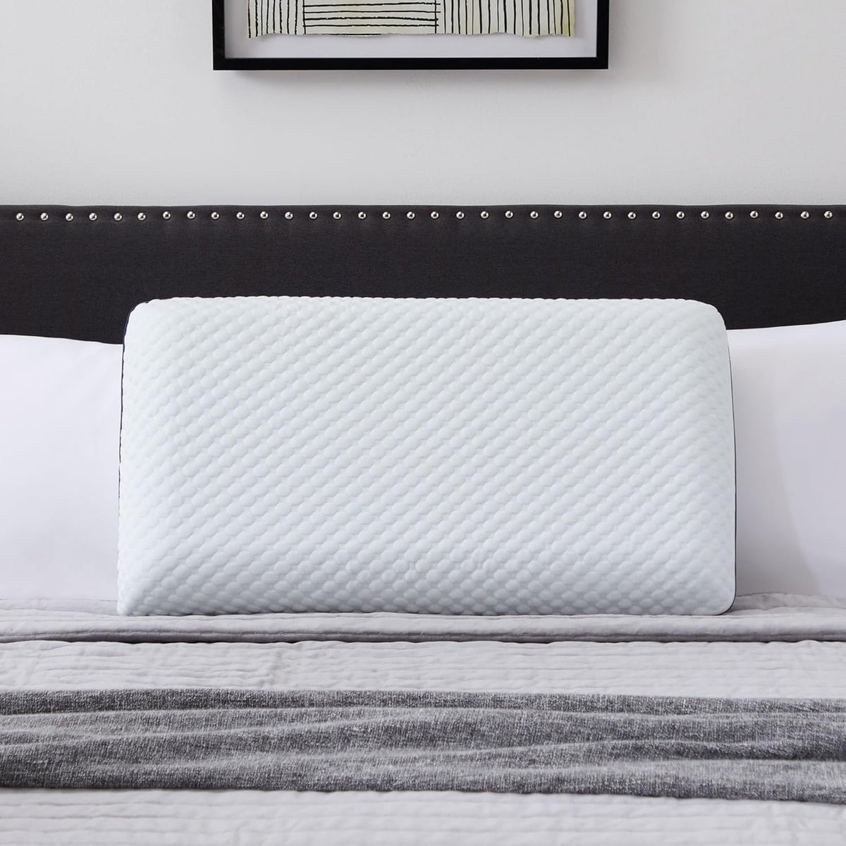 The quilted white pillow against a dark nailhead-trimmed headboard with white bedding