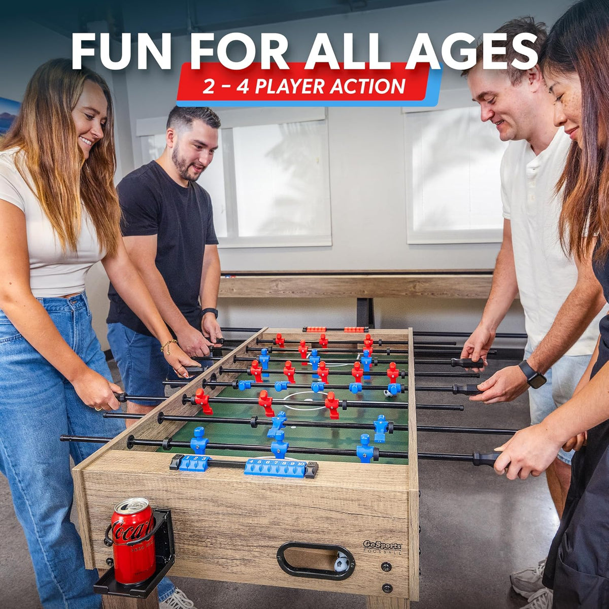 Four people playing at an oak-finish foosball table with a visible cup holder and blue sliding score beads