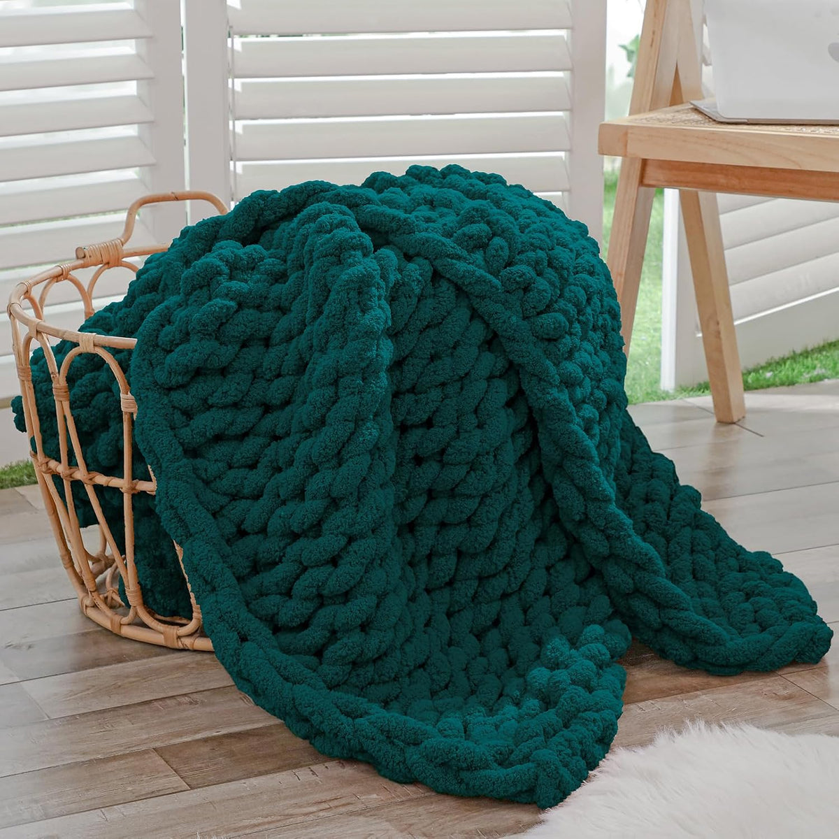 Deep teal chunky chenille throw overflowing a woven basket beside a wooden desk and shuttered window