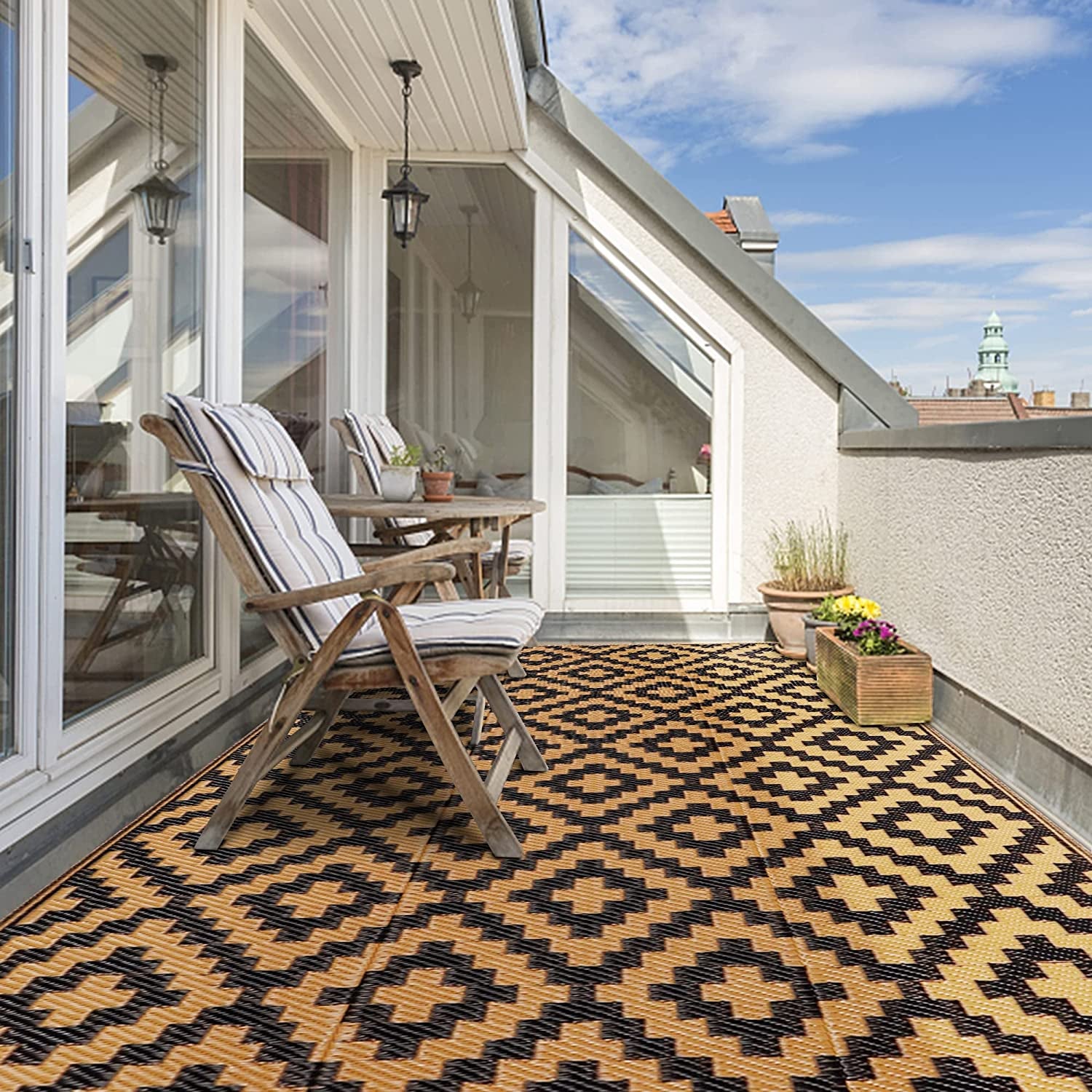 Balcony scene with two striped cushioned wooden chairs on a tan-and-black geometric outdoor rug and planters.