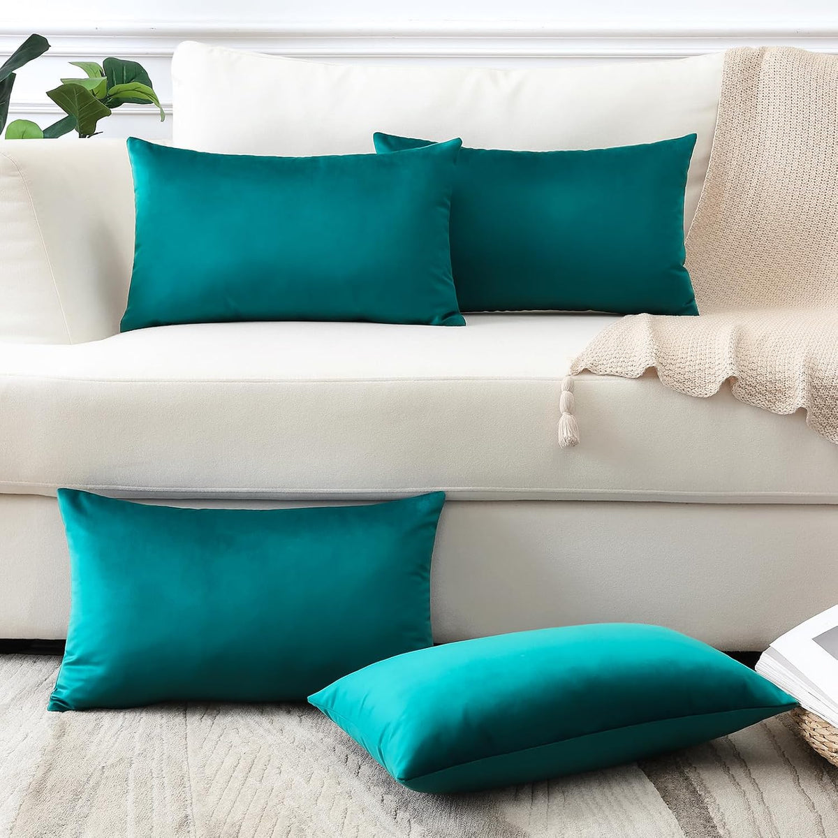 Rectangular and square teal velvet pillow covers staged on a cream sofa and floor.