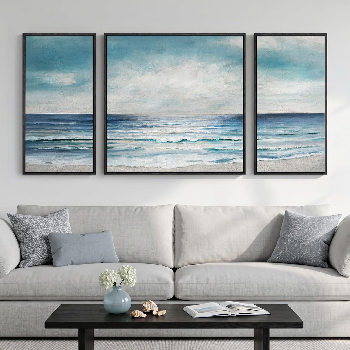 Three-panel seascape in soft blues and teal showing ocean and sky above a pale sofa and dark wood coffee table.