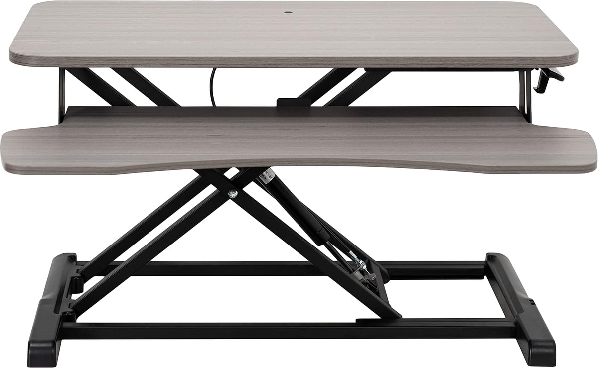 Front view of a two-tier standing desk converter with grey wood tops and black metal support frame.