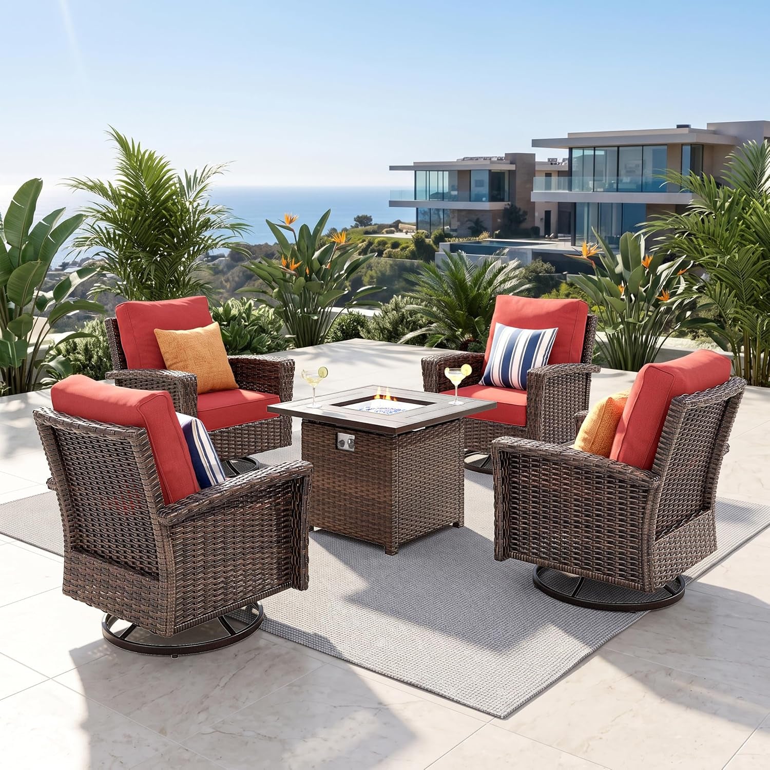 Outdoor wicker seating with red cushions on four swivel chairs gathered around a square fire table on a tiled terrace.