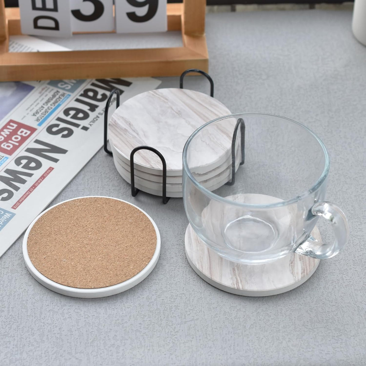 Overhead view of a glass mug on a coaster, a cork‑back coaster and a stacked set in a black holder on a gray table with a