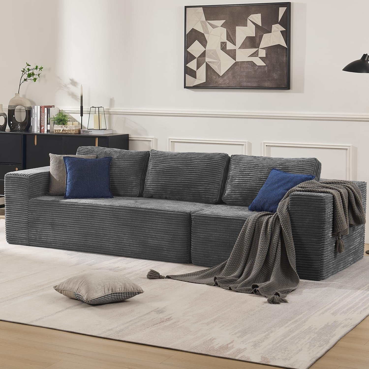Long charcoal L-shaped modular sectional with ribbed upholstery, three back cushions and blue accent pillows.