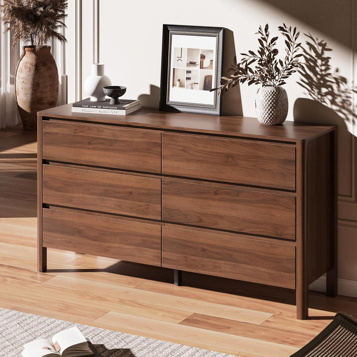 Angled side view of walnut 6-drawer dresser on a wood floor with tabletop decor and framed art