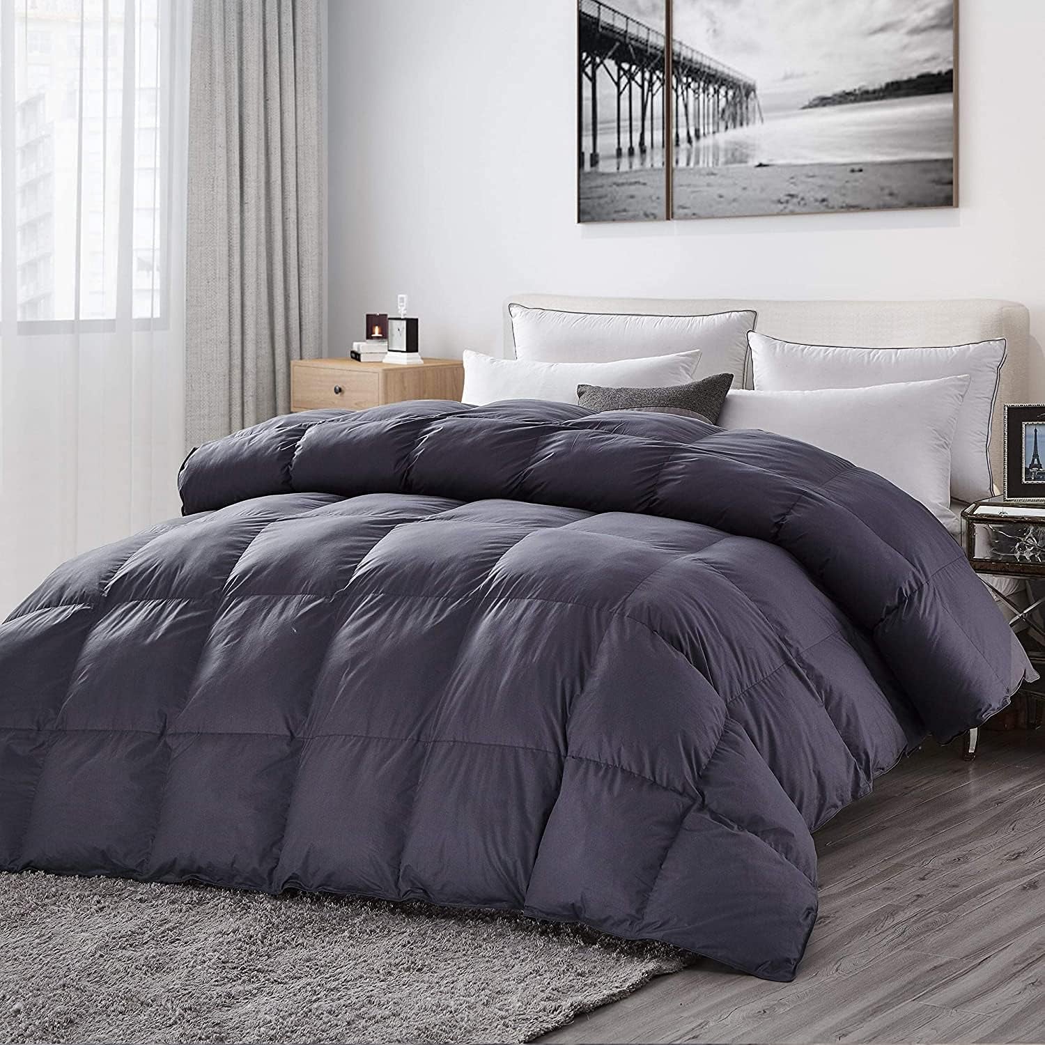 Angled view of a dark charcoal comforter draped over a bed with layered white pillows and rug