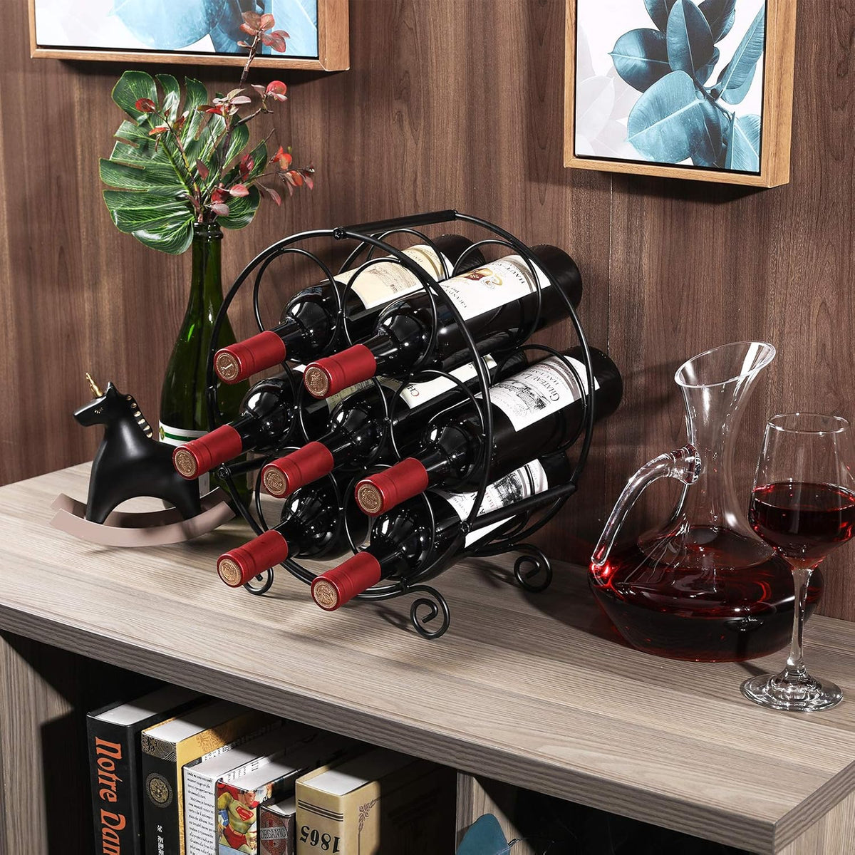 Black metal wine rack styled on a light wood shelf with a decanter, wine glass, and framed art.