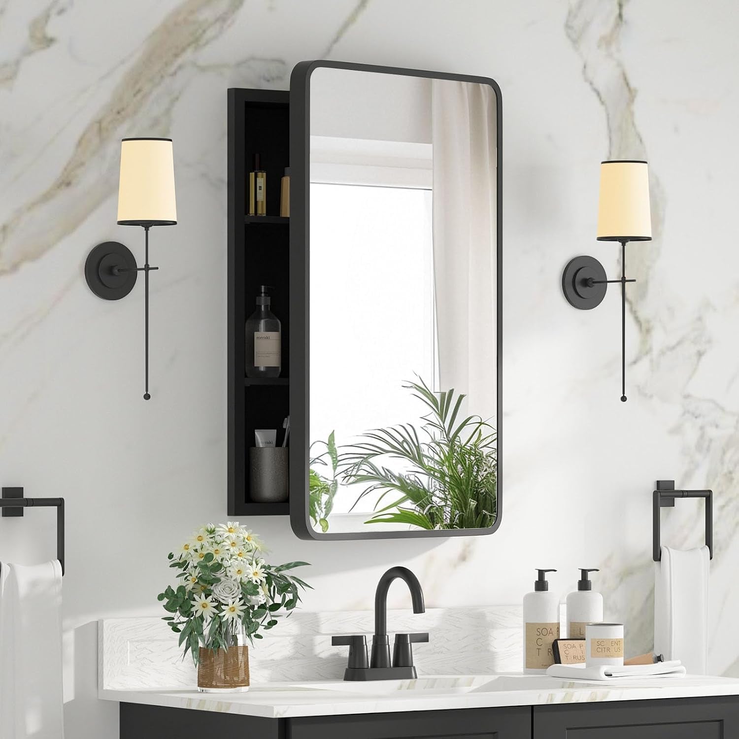 Angled view of a black-framed mirrored medicine cabinet mounted above a white sink with decorative plants.