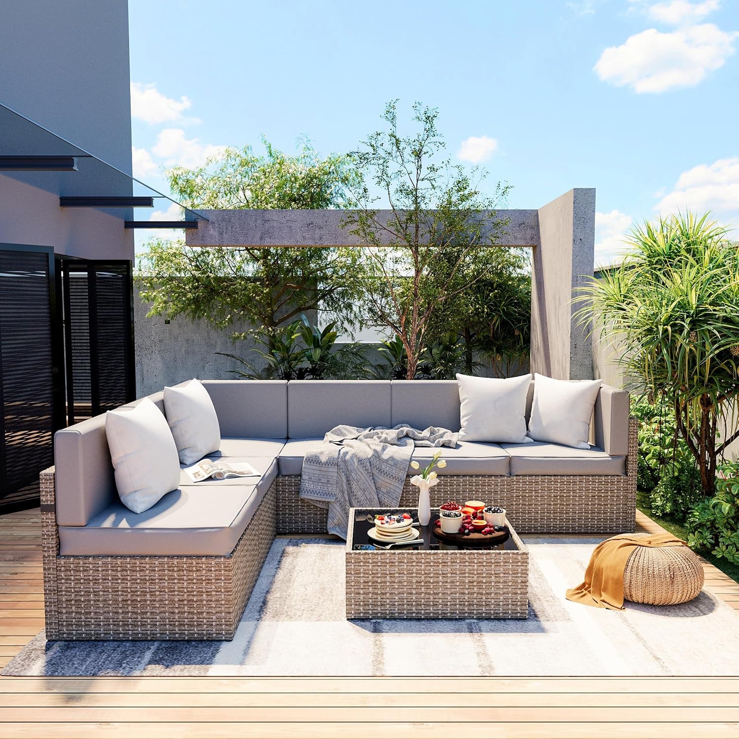 Outdoor corner wicker sectional with light gray cushions, low wicker coffee table and woven pouf on a wood deck.
