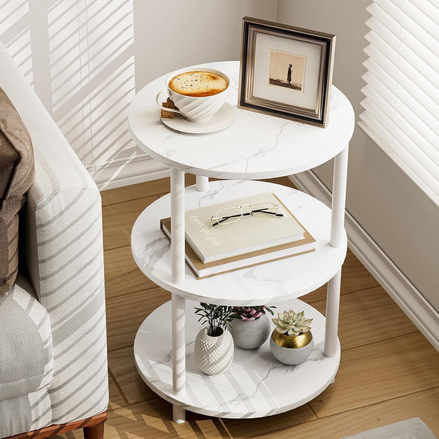 White three-tier round side table next to a couch holding a framed photo, cup and books