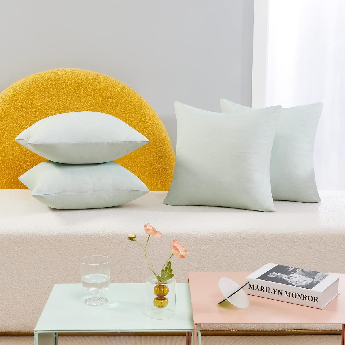 Four pale mint pillow covers with two stacked and two standing against a yellow textured prop