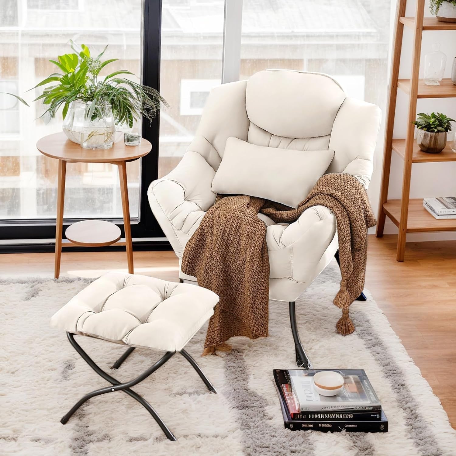 Cream-colored cushioned lounge chair with ottoman and a brown throw draped over the arm in front of a window.
