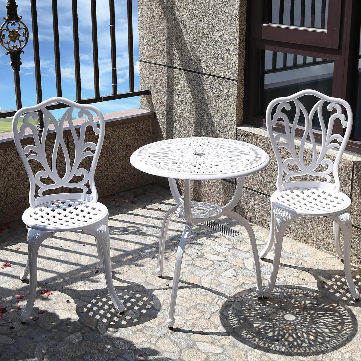 White cast-aluminum bistro table and two chairs on a sunny balcony with lattice seat pattern.
