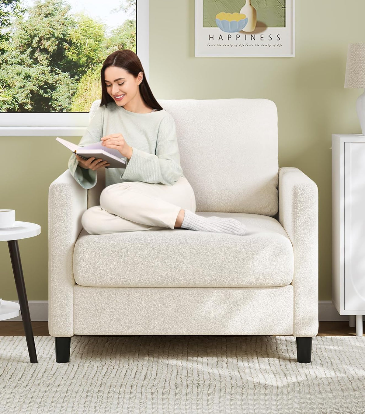 Front view of a cream teddy fabric loveseat in a sunlit living room with a woman reading on it.