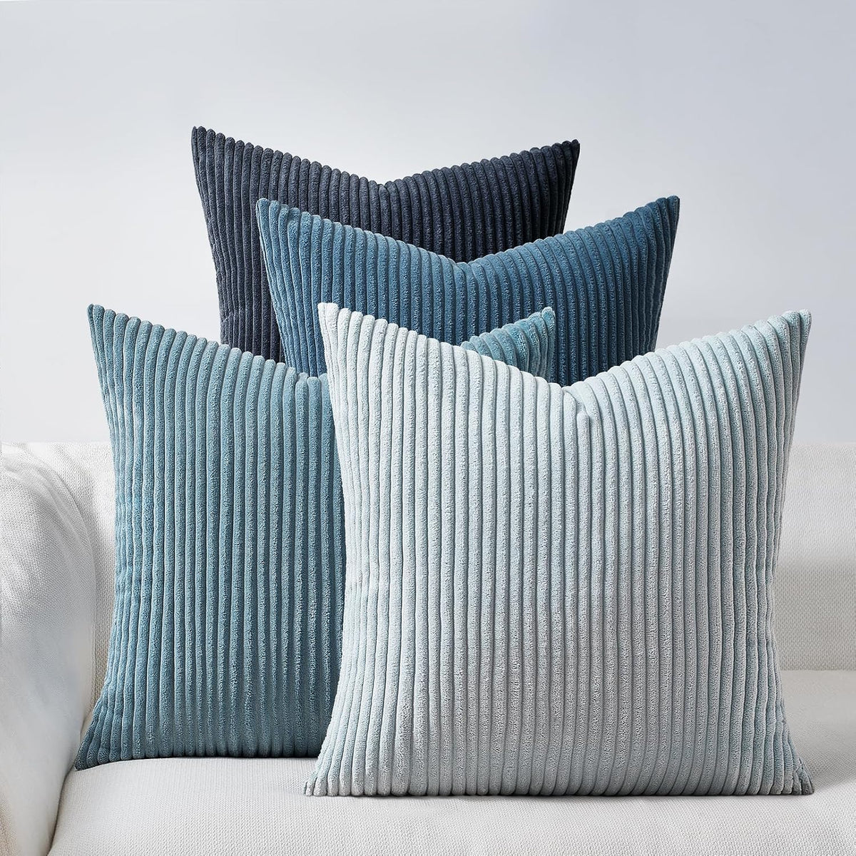 Five vertical‑corded pillows in dark navy, teal and pale blue displayed on a couch