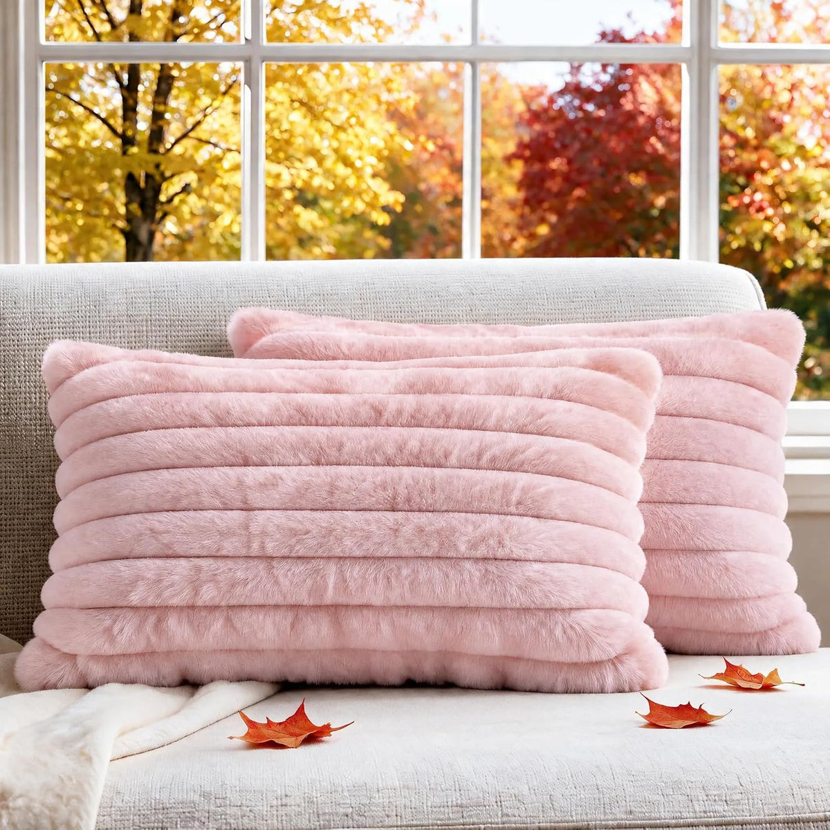 Two cream-pink faux fur ribbed throw pillow covers on a light sofa with autumn leaves by the window