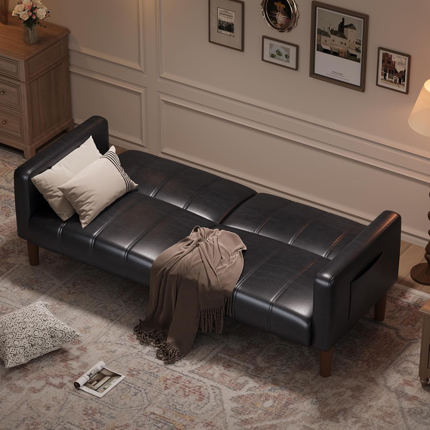 Black faux-leather futon shown flat as a bed in a styled living room with pillows and a throw.