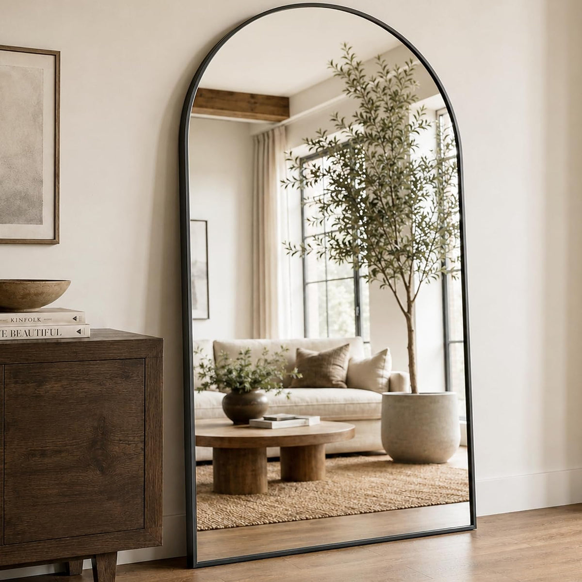 Close side view of an arched mirror with a dark frame showing a living room reflected in the glass.