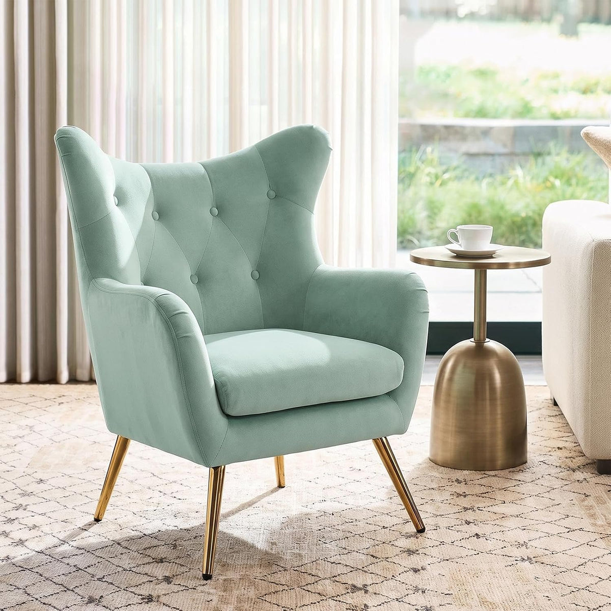 Single mint-green wingback chair next to a small gold side table with a cup, sofa edge visible