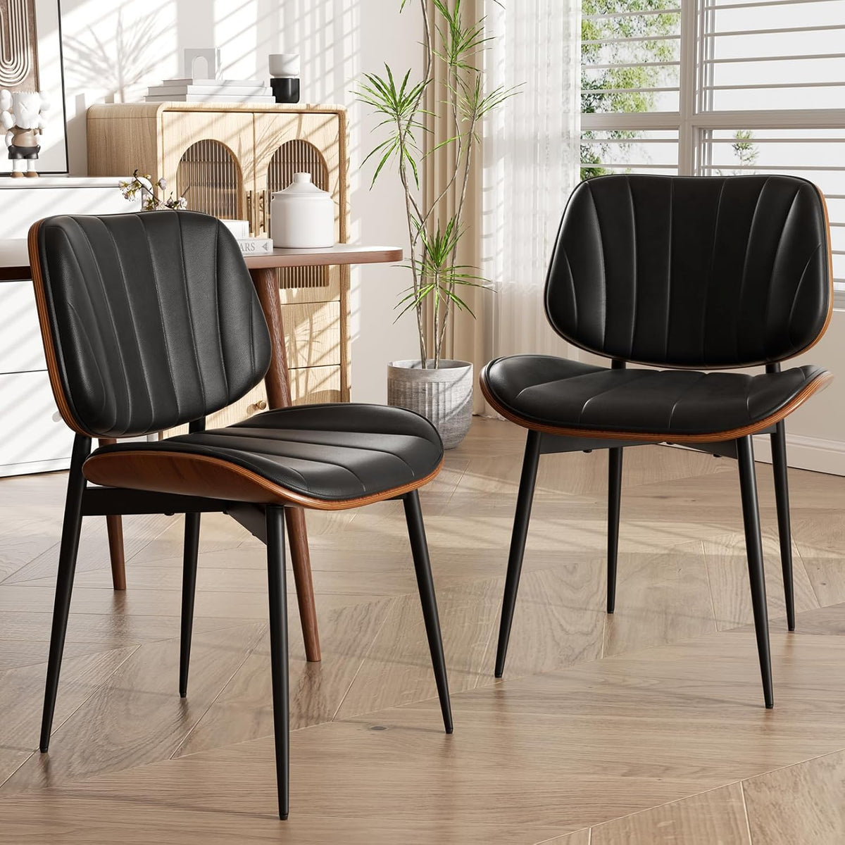 Two black faux leather dining chairs with walnut bentwood trim angled front view in a sunlit dining room