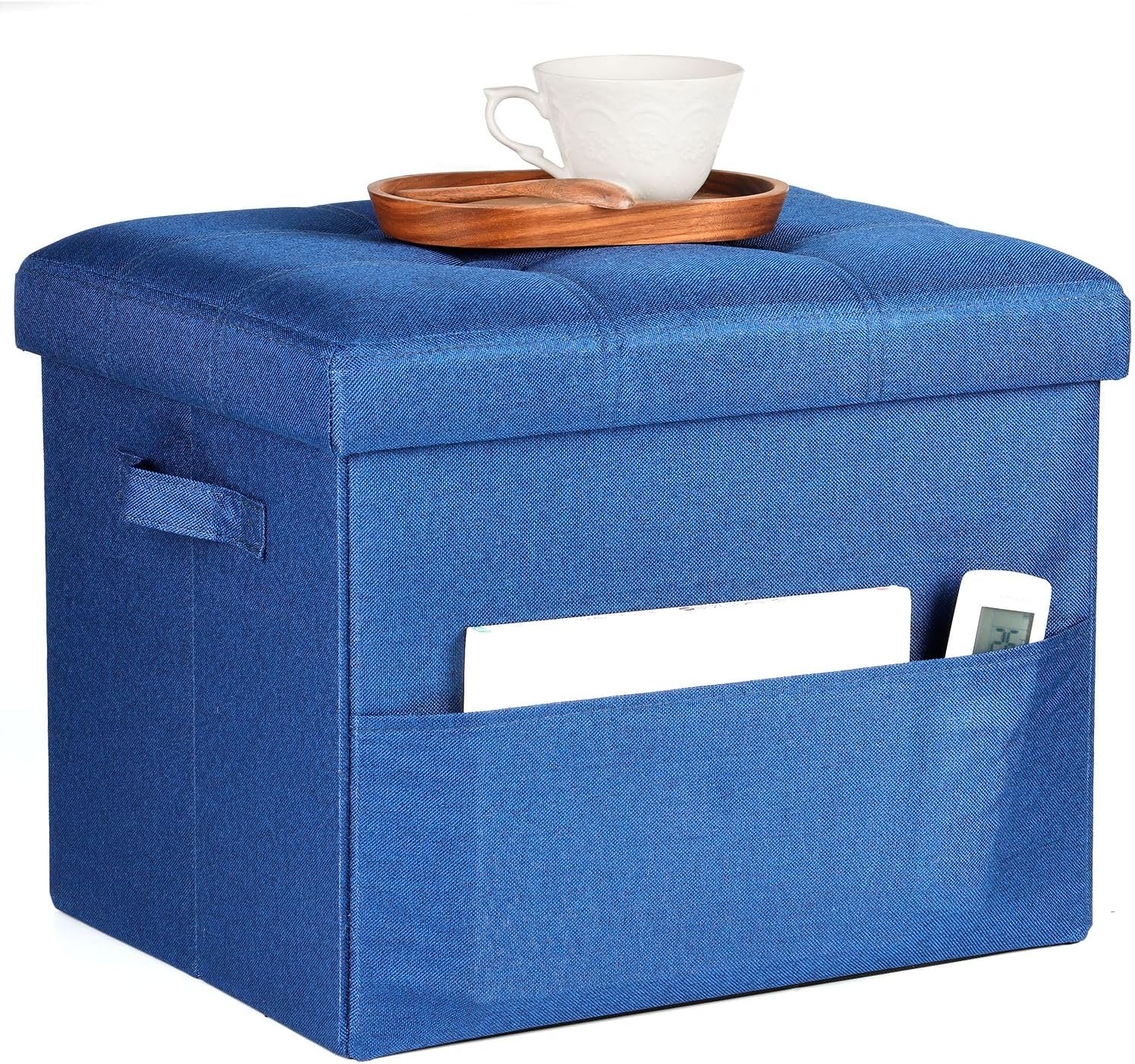 Blue fabric storage ottoman with tufted top, side handle and front pocket holding a tablet and remote; tray and cup on lid