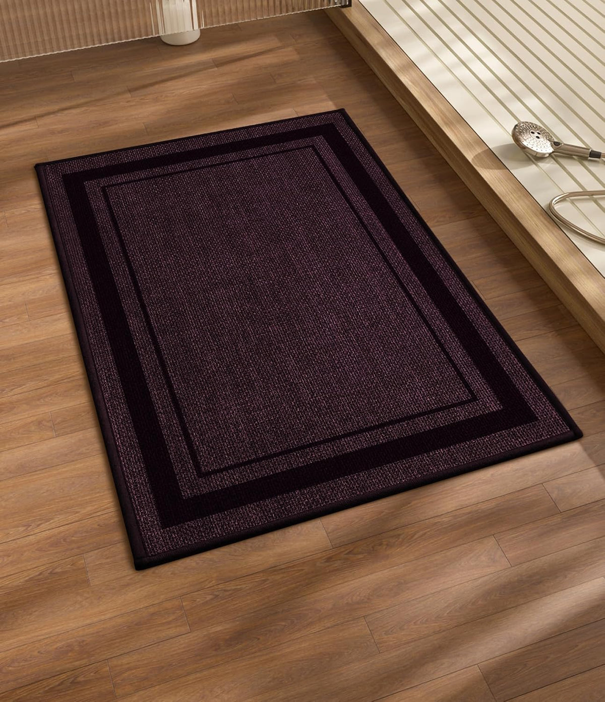 Deep plum rectangular bath mat with contrasting darker inner and outer borders on wood floor