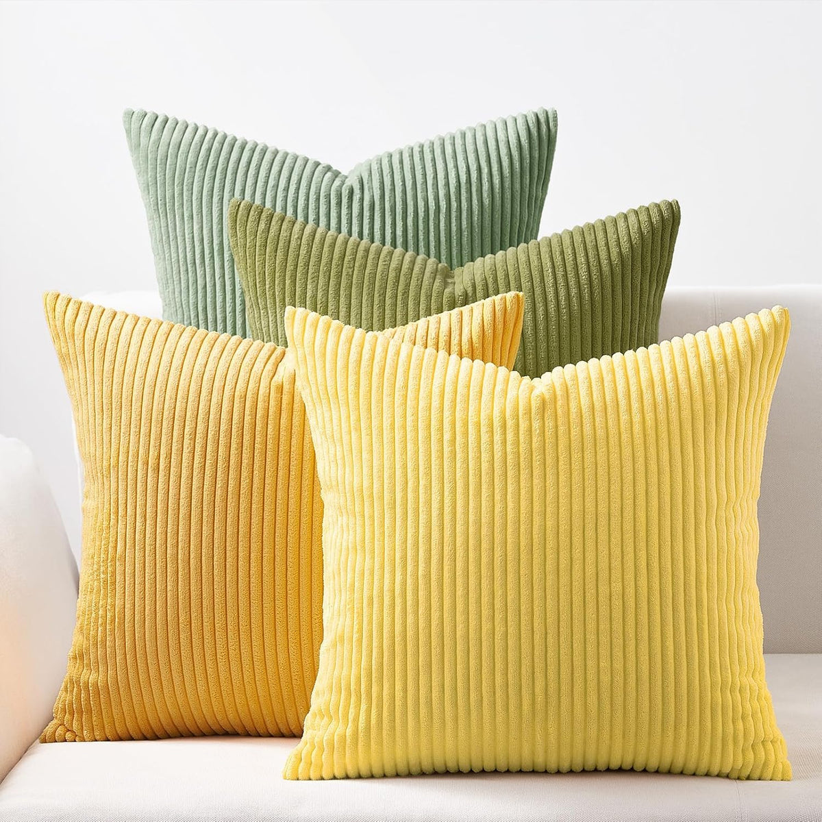 Four corduroy ribbed square pillows in yellow and green tones arranged on a light sofa