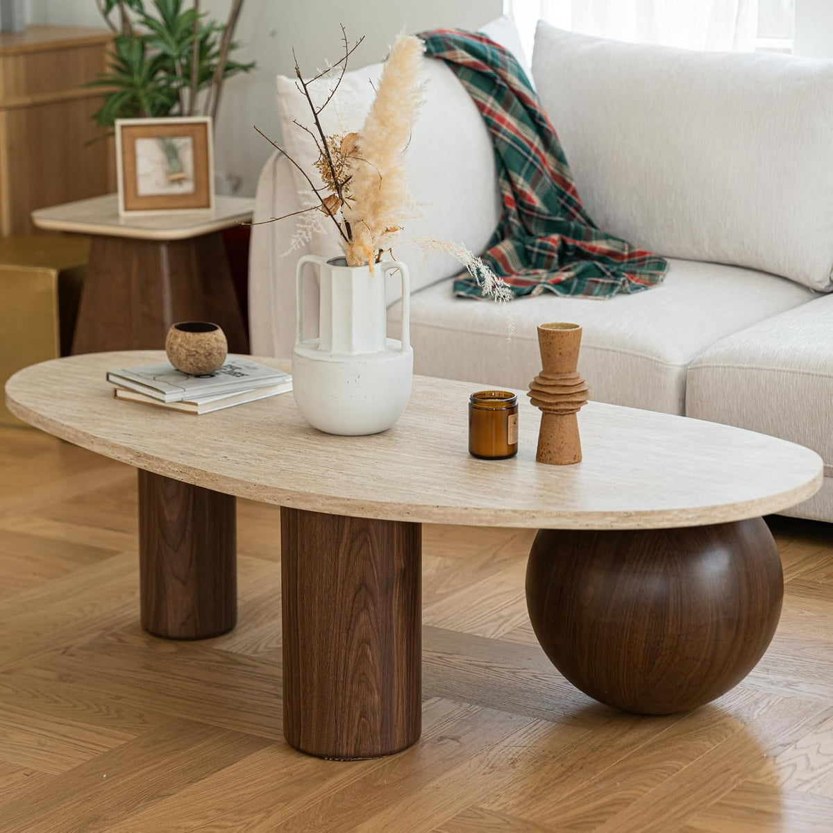 Beige travertine-style oval coffee table with walnut-finish cylindrical and spherical legs, angled front view in a livingroom