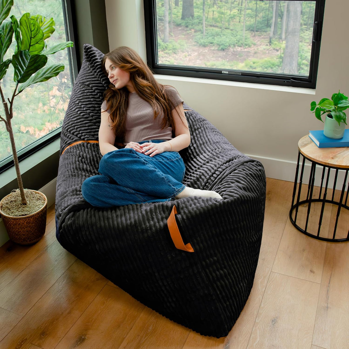 Woman reclining on a large dark corded plush bean bag by a window and side table