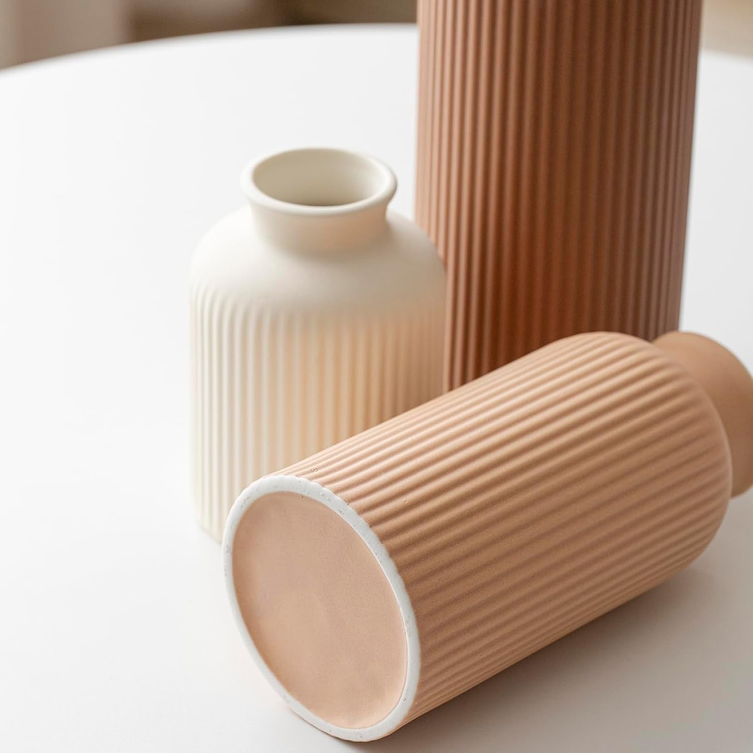 Close detail showing the unglazed base and vertical ribbing on a light terracotta vase with two upright vases behind